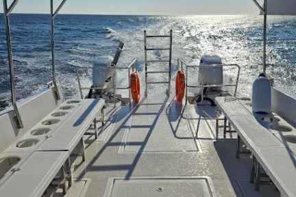 View from boat deck with benches, ocean waves, and sunny sky.