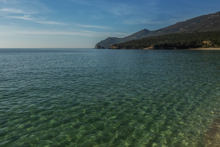 Clear sea with distant hills under a blue sky.