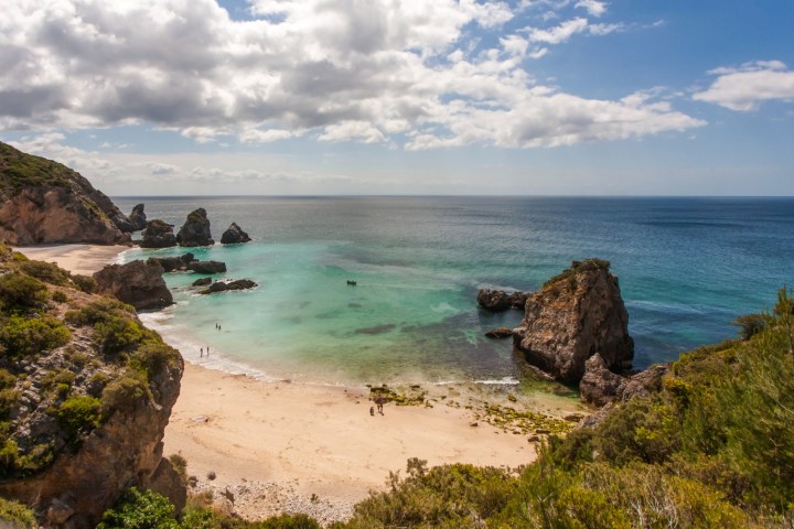 Scenic beach with rocky cliffs, turquoise water, and a cloudy sky.