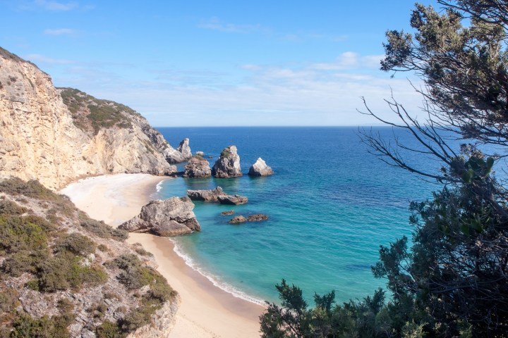 Coastal view of a sandy beach with rocky cliffs and blue ocean.