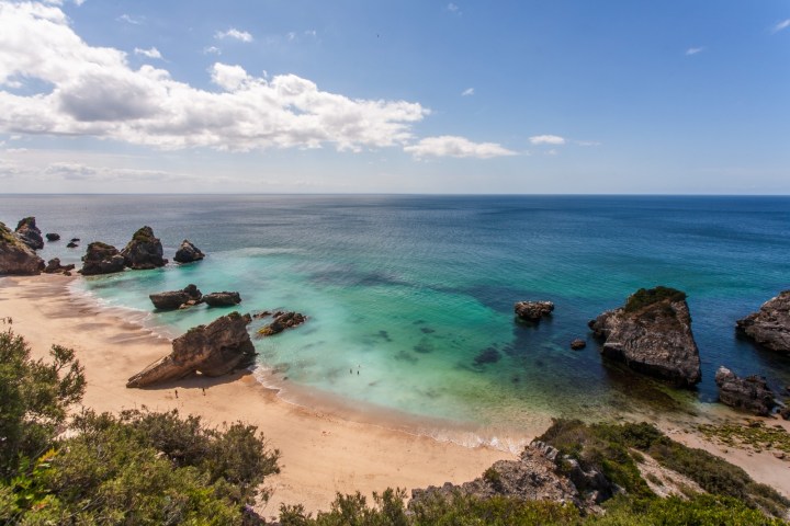 Scenic beach with rocks, turquoise water, and blue sky.