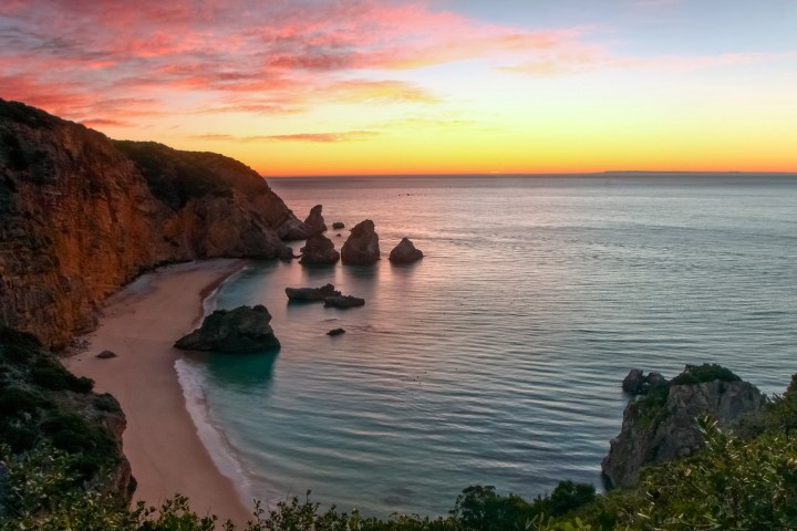 Scenic beach at sunrise with cliffs and rock formations in the ocean.