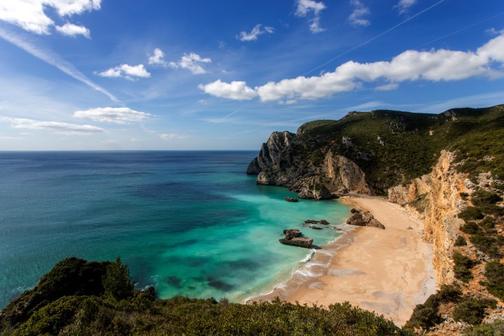 Cliffside beach with turquoise water and clear blue sky.