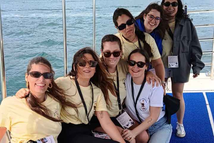 Group of seven people smiling on a boat with a scenic background.