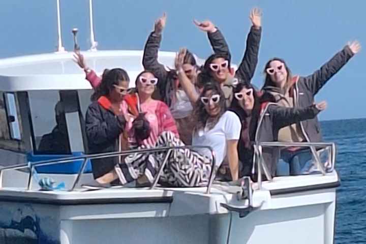 Group of people waving on a boat with a flag in the ocean.